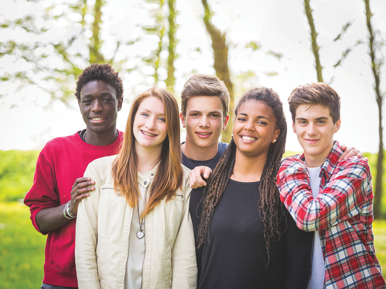 youthful epople of various background standing in front of a wooded, grassy background. 